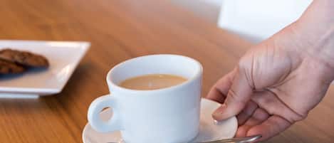 A white cup of coffee on a saucer with a spoon, held by a hand.