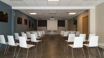 A conference room with rows of white chairs, a projector screen, and a presentation podium.