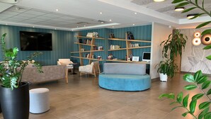 A modern lobby with a blue wall, a bookshelf, seating areas, and a TV.