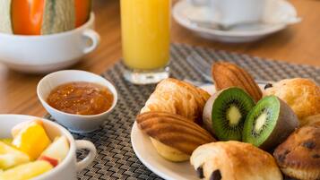 Een ontbijttafel met croissants, kiwi plakjes en een glas sinaasappelsap op een geweven placemat.
