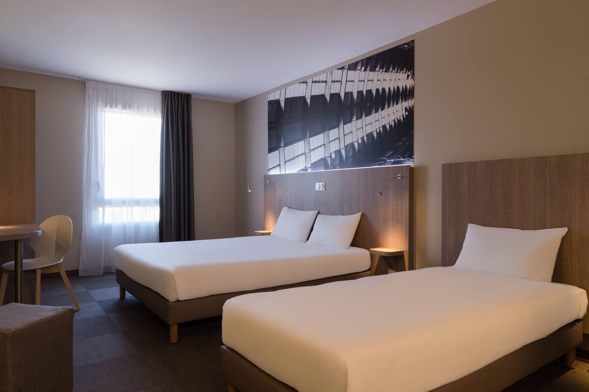 Habitación de hotel con dos camas, un escritorio, una silla y un cuadro abstracto grande en la pared.