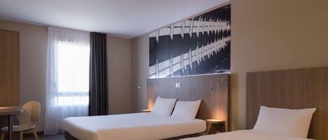 A hotel room with two beds, a desk, and a chair.