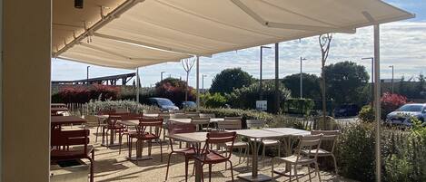 An outdoor café with tables and chairs under a large canopy.