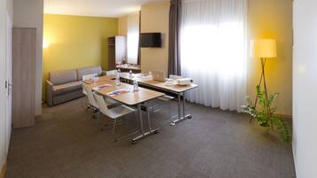 A modern hotel room with a dining area, a sofa, a TV, and a plant.