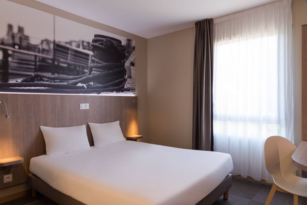 Una habitación de hotel con una cama grande, una mesita de noche, una silla y una obra de arte colgada en la pared.