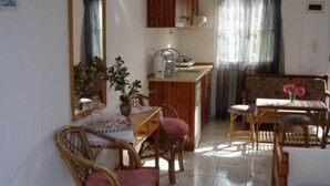 A cozy dining area with wooden furniture, a small kitchen area with a coffee maker, and a window with curtains. - Villa Thalia (Agios Nikolaos)
