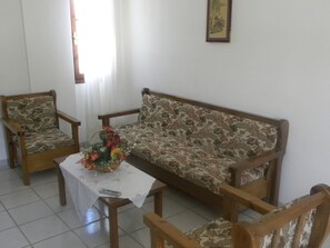 A living room with a sofa, two armchairs, a coffee table with a floral tablecloth, and a vase with flowers. - Villa Thalia (Agios Nikolaos)