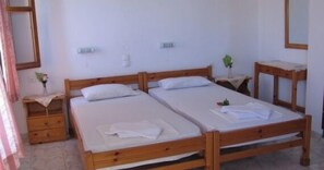 A room with two wooden beds, a small bedside table with a plant, and a mirror on the wall.