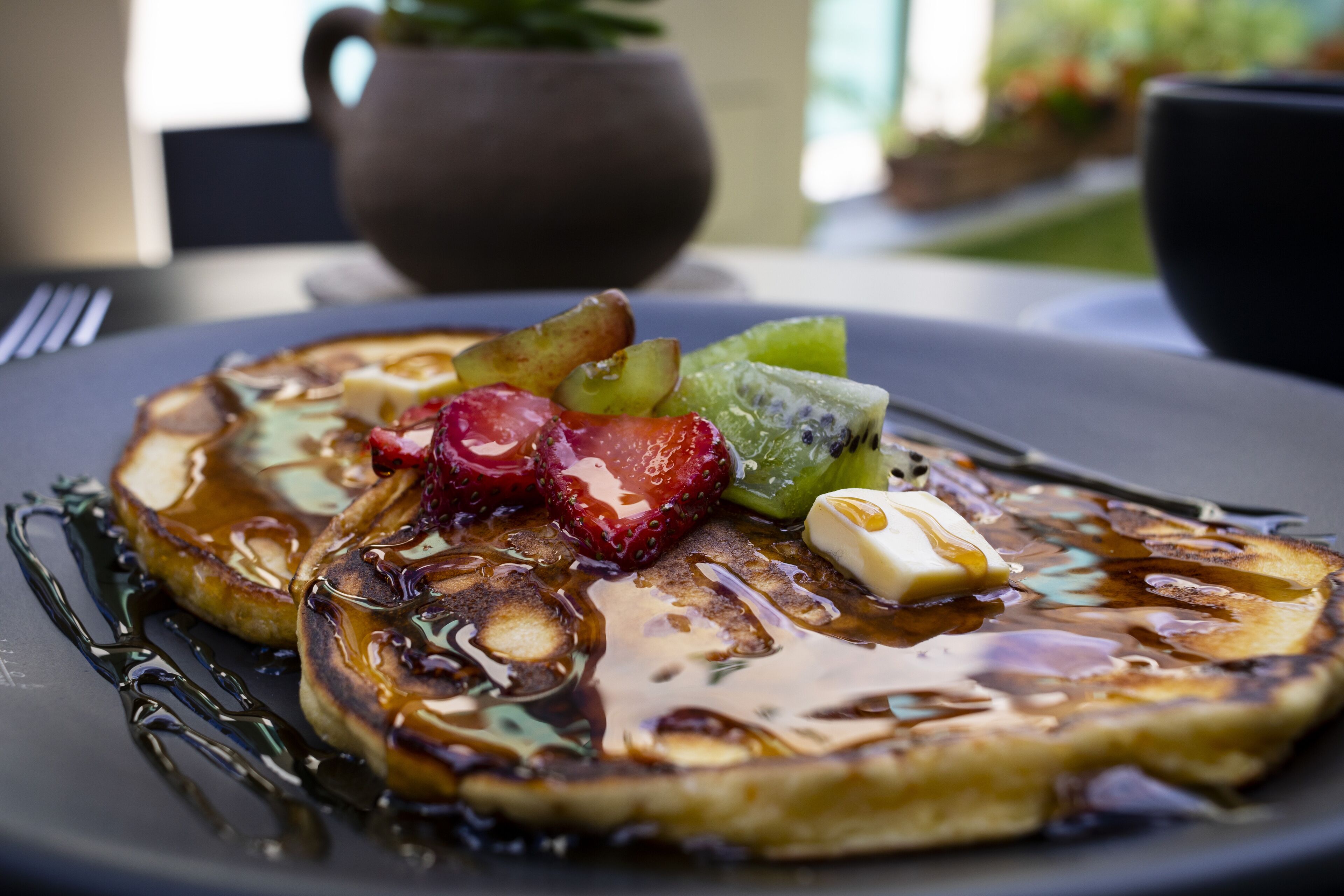 A breakfast plate with pancakes, fruit, and syrup.