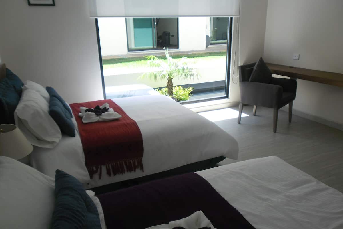 Une chambre d’hôtel moderne dotée d’un grand lit, d’un bureau et offrant une vue sur un espace extérieur verdoyant.