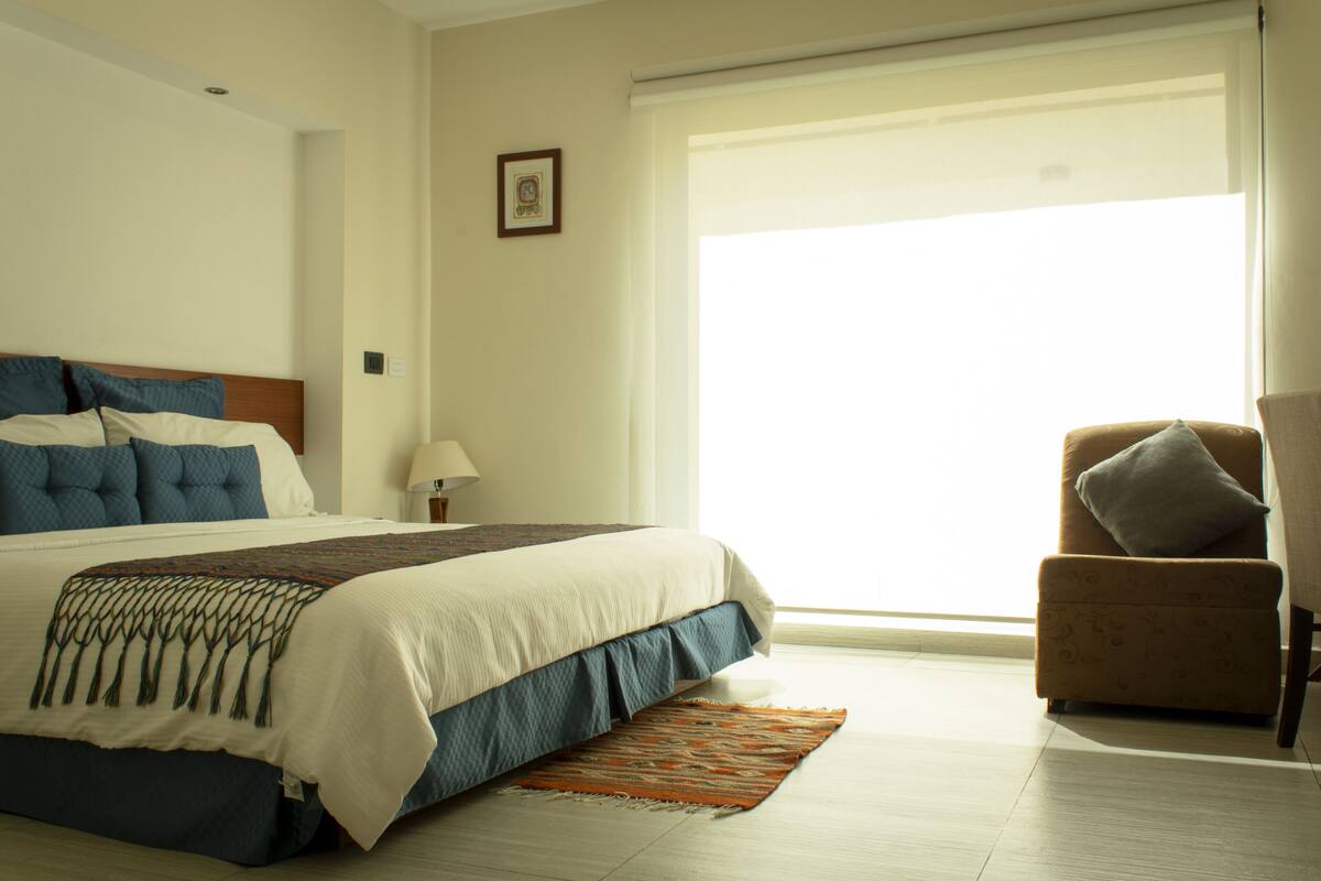 Une chambre d’hôtel avec un grand lit, une chaise, une fenêtre et un tableau au mur.