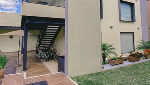 Een modern huis met twee verdiepingen, een ruim balkon, een trap naar de bovenverdieping en een kleine tuin met potplanten.