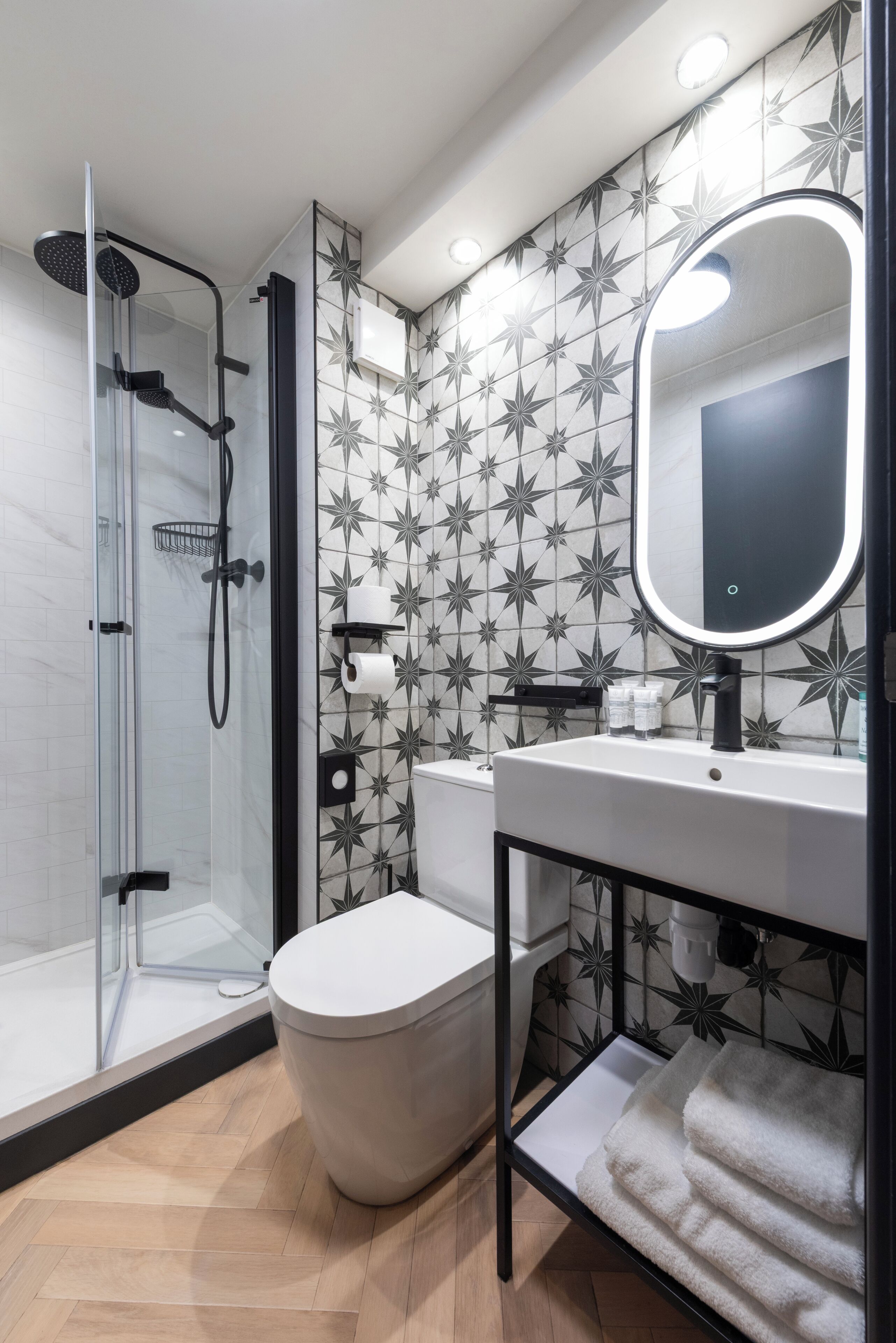 A modern bathroom with a glass shower enclosure, a toilet, a sink with a mirror, and a towel rack.