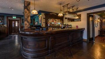 A bar area with a central bar counter, overhead lighting, and a bar stocked with bottles.