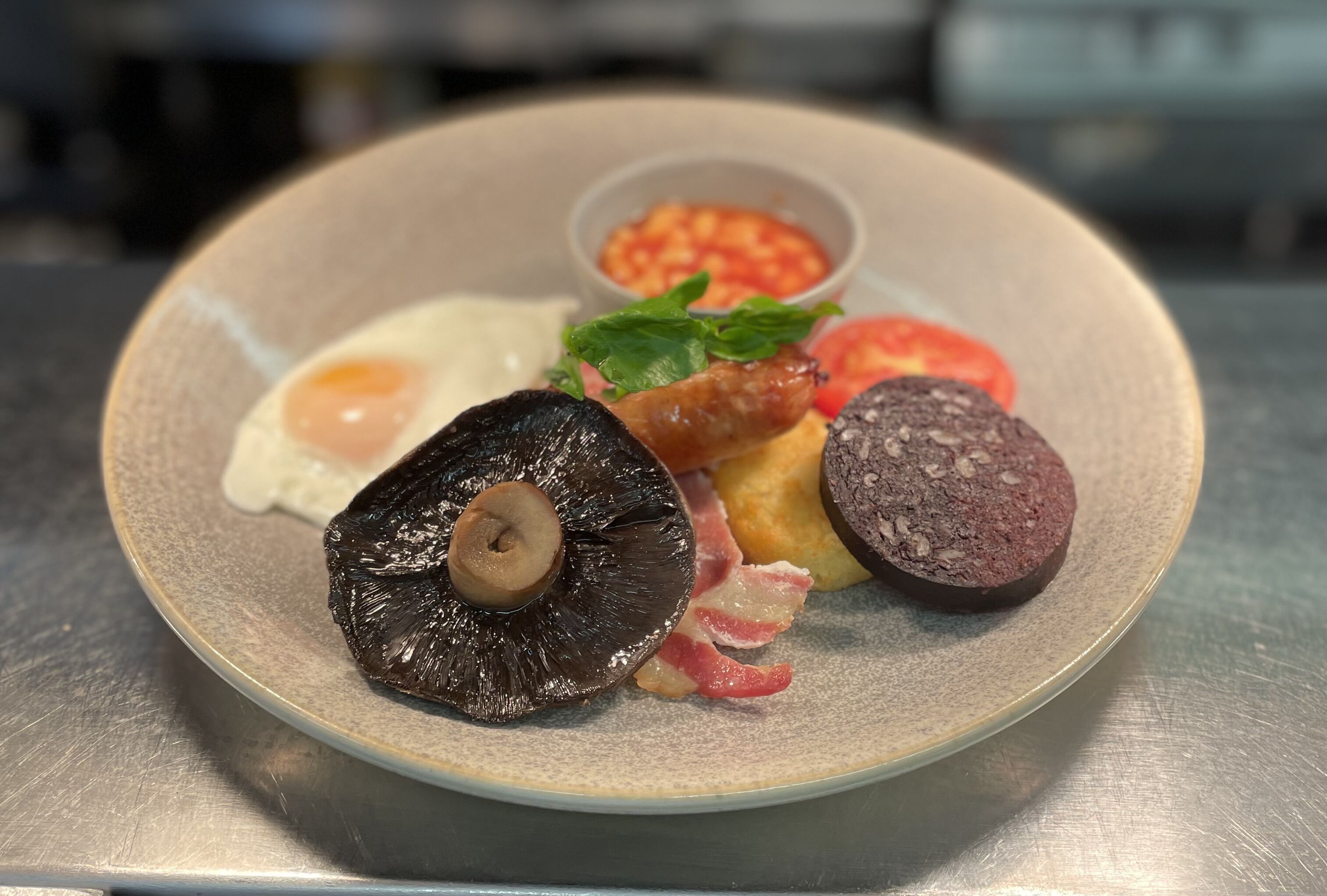 A plate with a variety of foods including an egg, mushrooms, bacon, sausage, and a tomato.