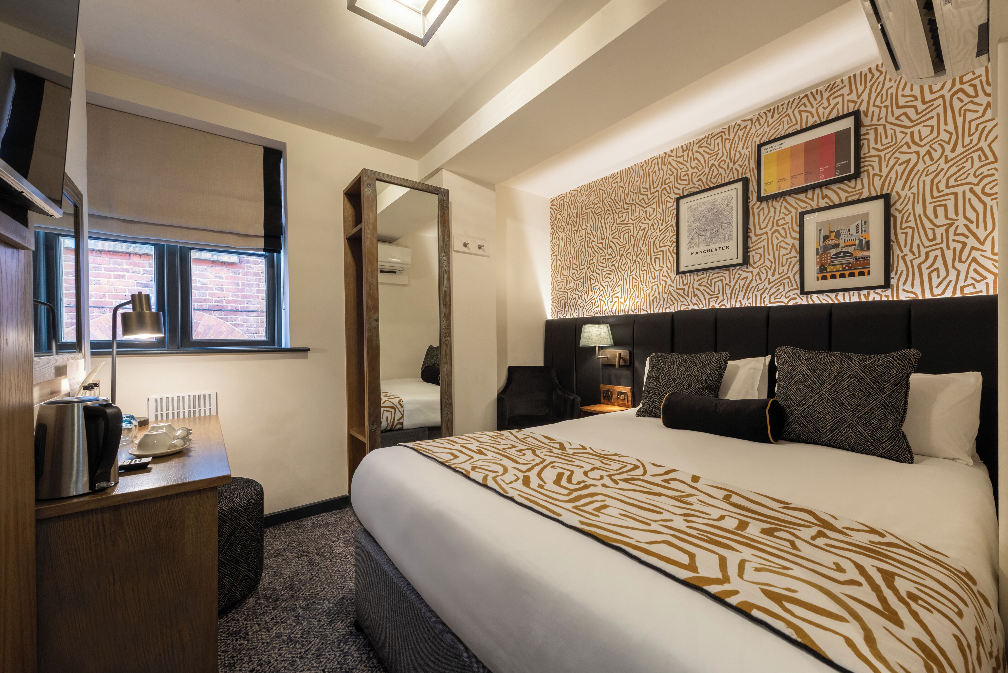Habitación de hotel con una cama grande, un escritorio con hervidor, un espejo y una ventana con persianas.