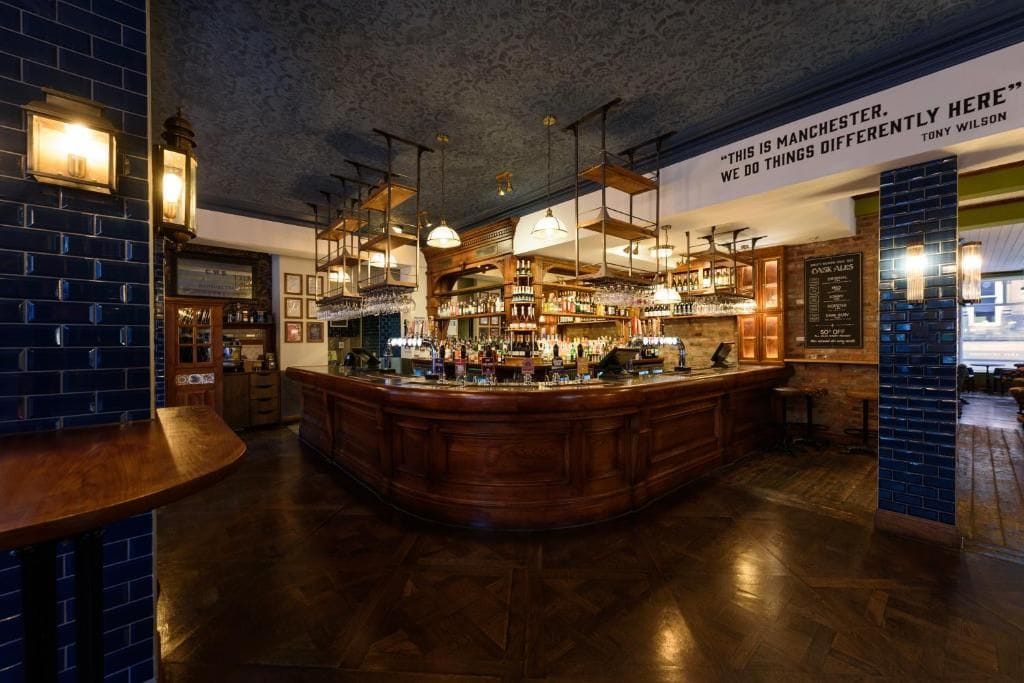 Zona de bar con mostrador de madera, luces colgantes y pared de ladrillo.