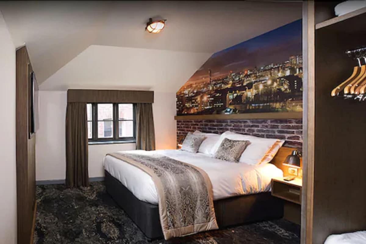 A bedroom with a bed, a window with curtains, a cityscape mural, and a hanging clothes rack.