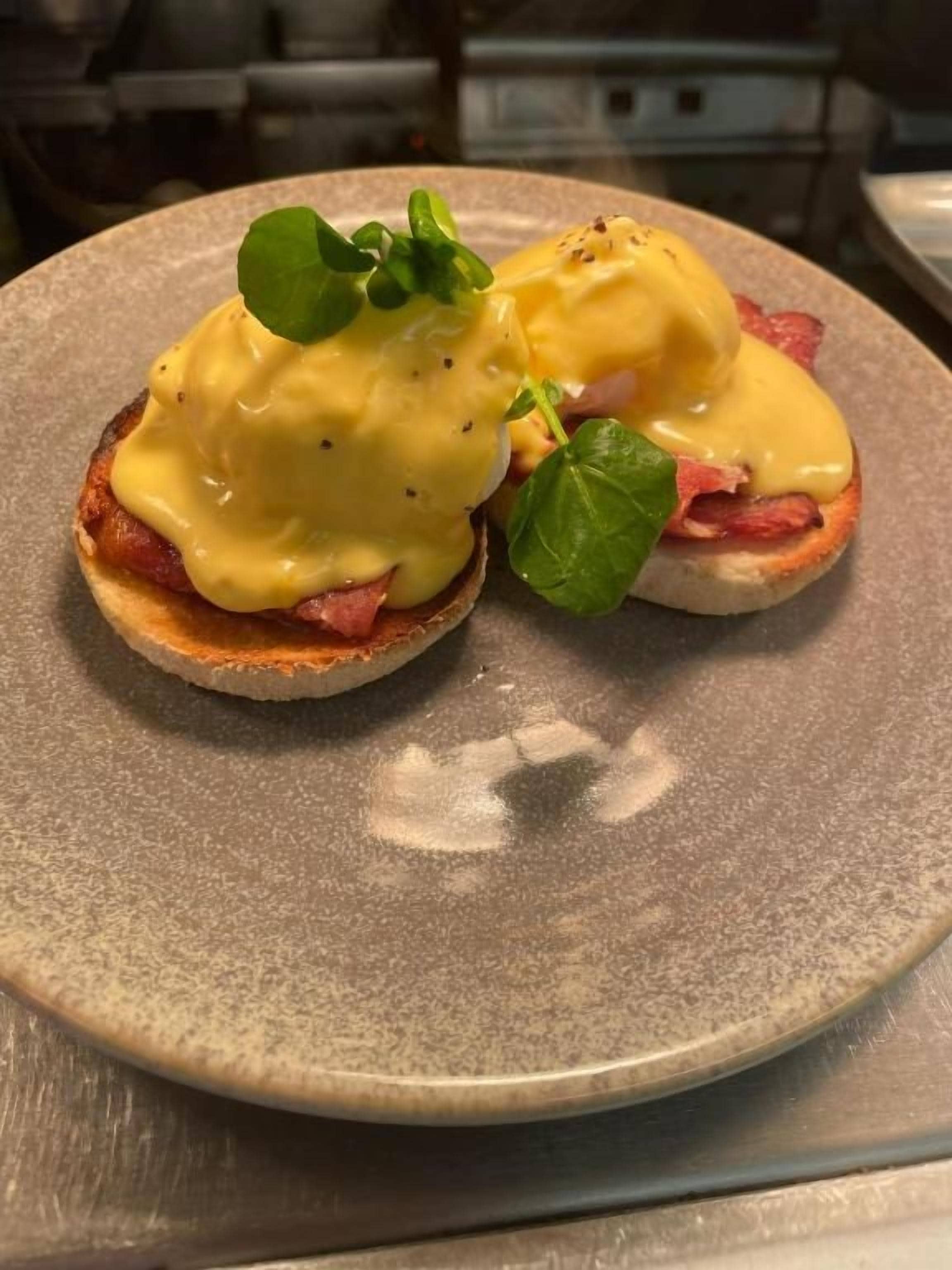 A plate with two eggs benedict sandwiches topped with hollandaise sauce and garnished with a leaf.