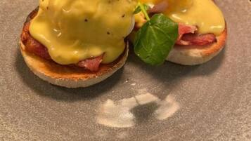 A plate with two eggs benedict sandwiches topped with hollandaise sauce and garnished with a leaf.