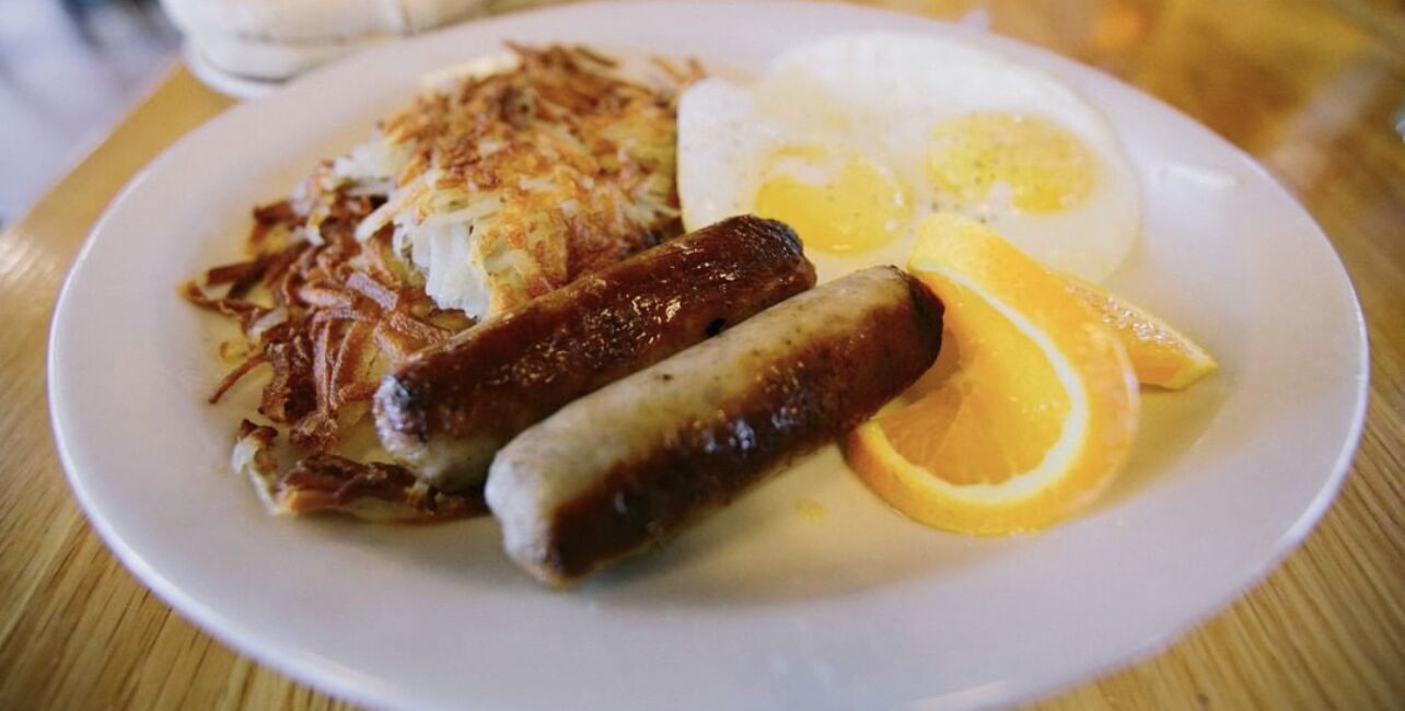 Un plato con hash browns, salchichas, un huevo frito y una rodaja de naranja.