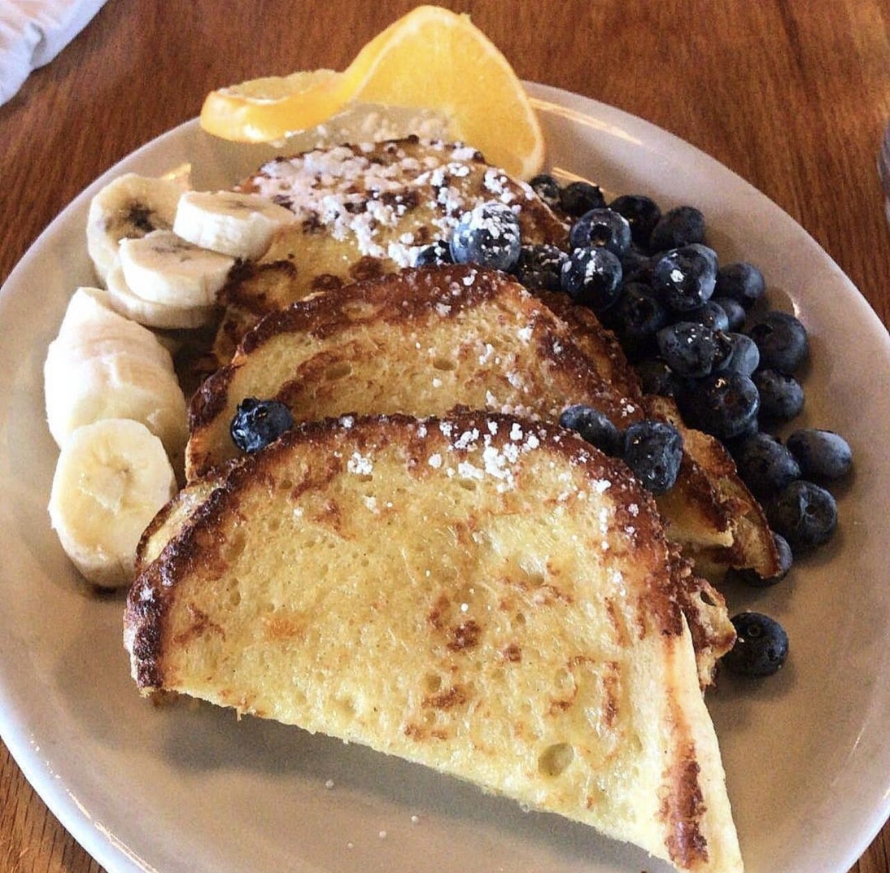 En tallrik med fransk toast, skivade bananer, blåbär och en klyfta citron.
