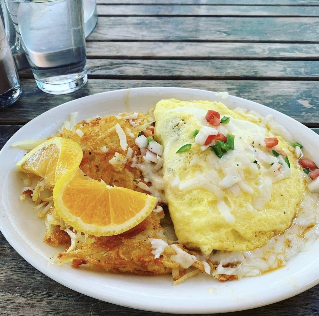 A plate with an omelette, fried potatoes, and a slice of orange on a wooden table.
