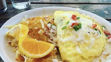 A plate with an omelette, fried potatoes, and a slice of orange on a wooden table.