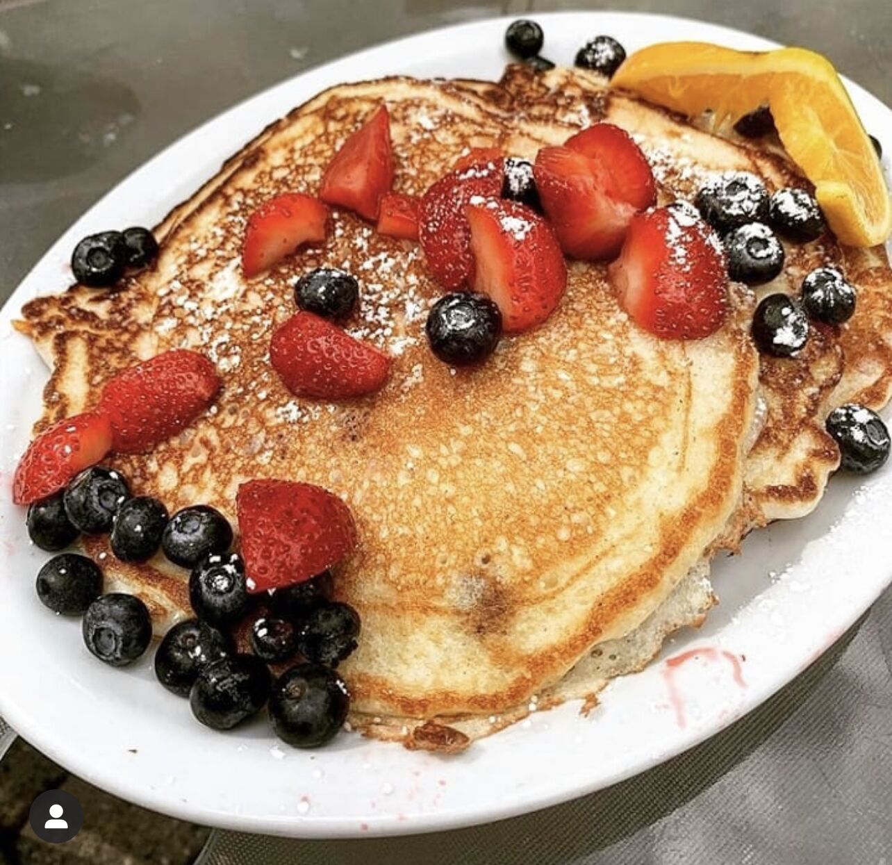 Een bord pannenkoeken met aardbeien, bosbessen en een sinaasappelschijf.