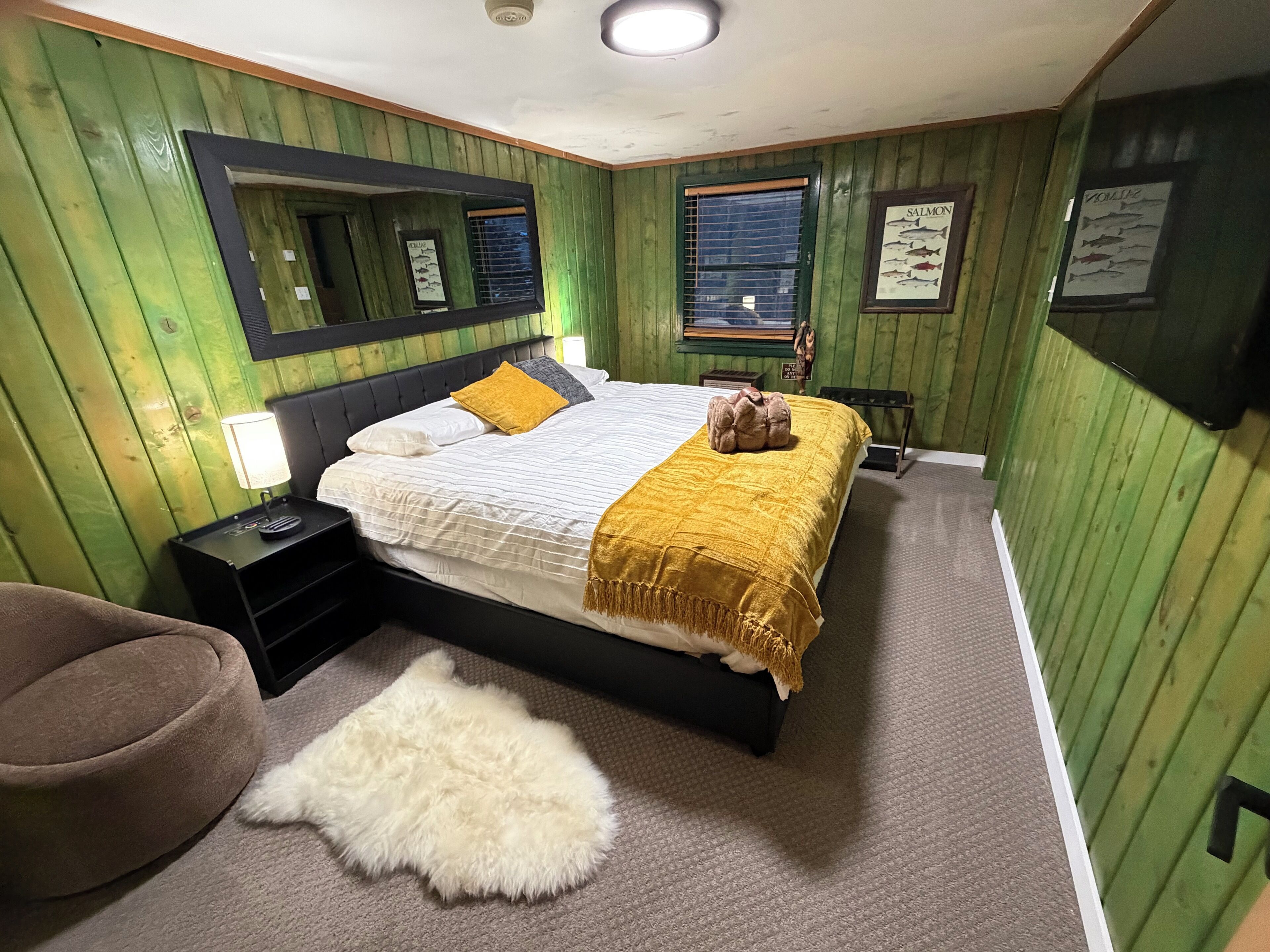 A bedroom with a bed, a nightstand, a mirror, a window, and green wooden walls.