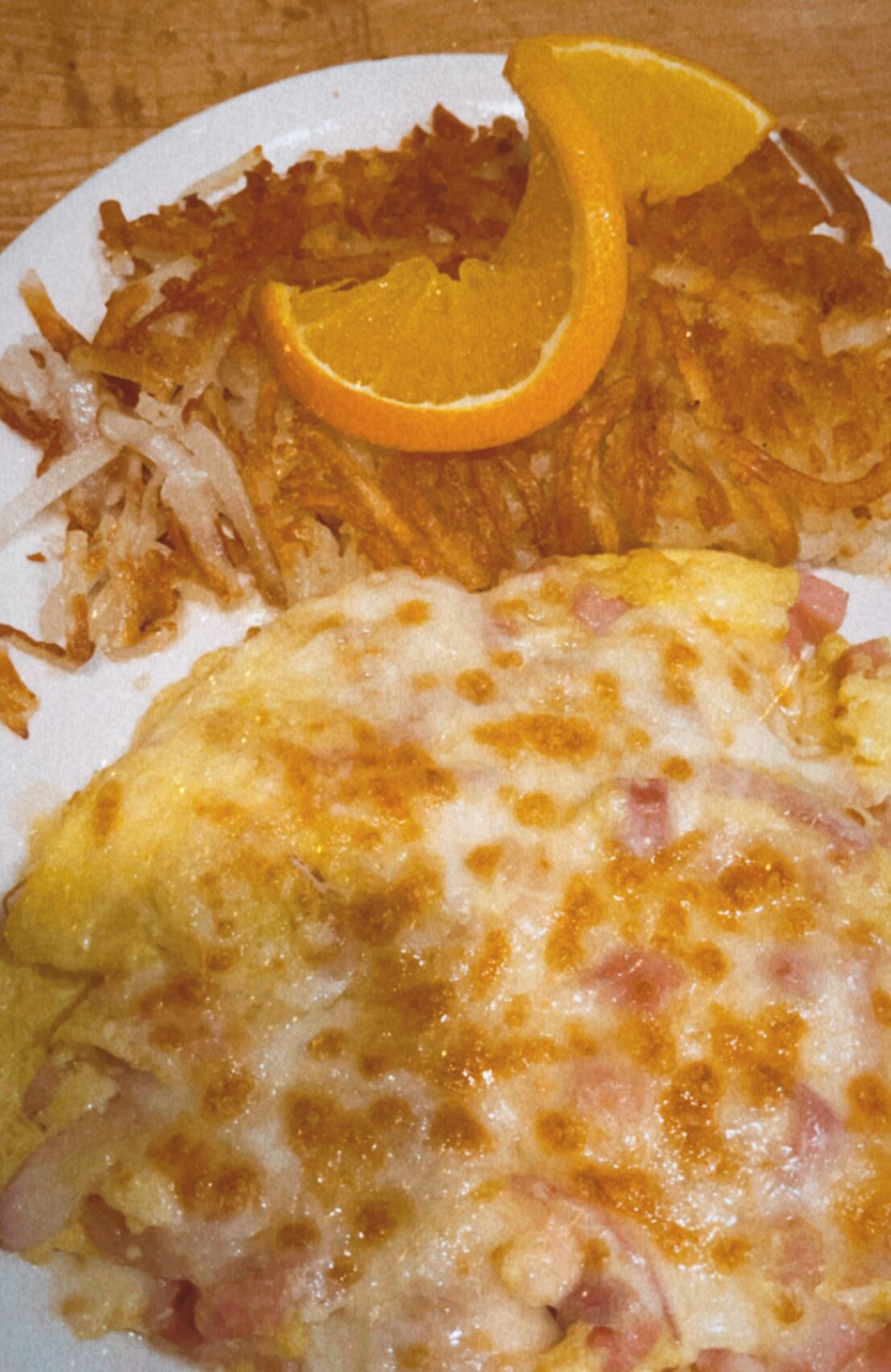 A plate with a fried egg, hash browns, and a slice of orange.