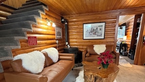 A log cabin interior with a brown leather sofa, a wooden coffee table, and a staircase leading to an upper level. - Silver Fork Lodge and Restaurant (Brighton)