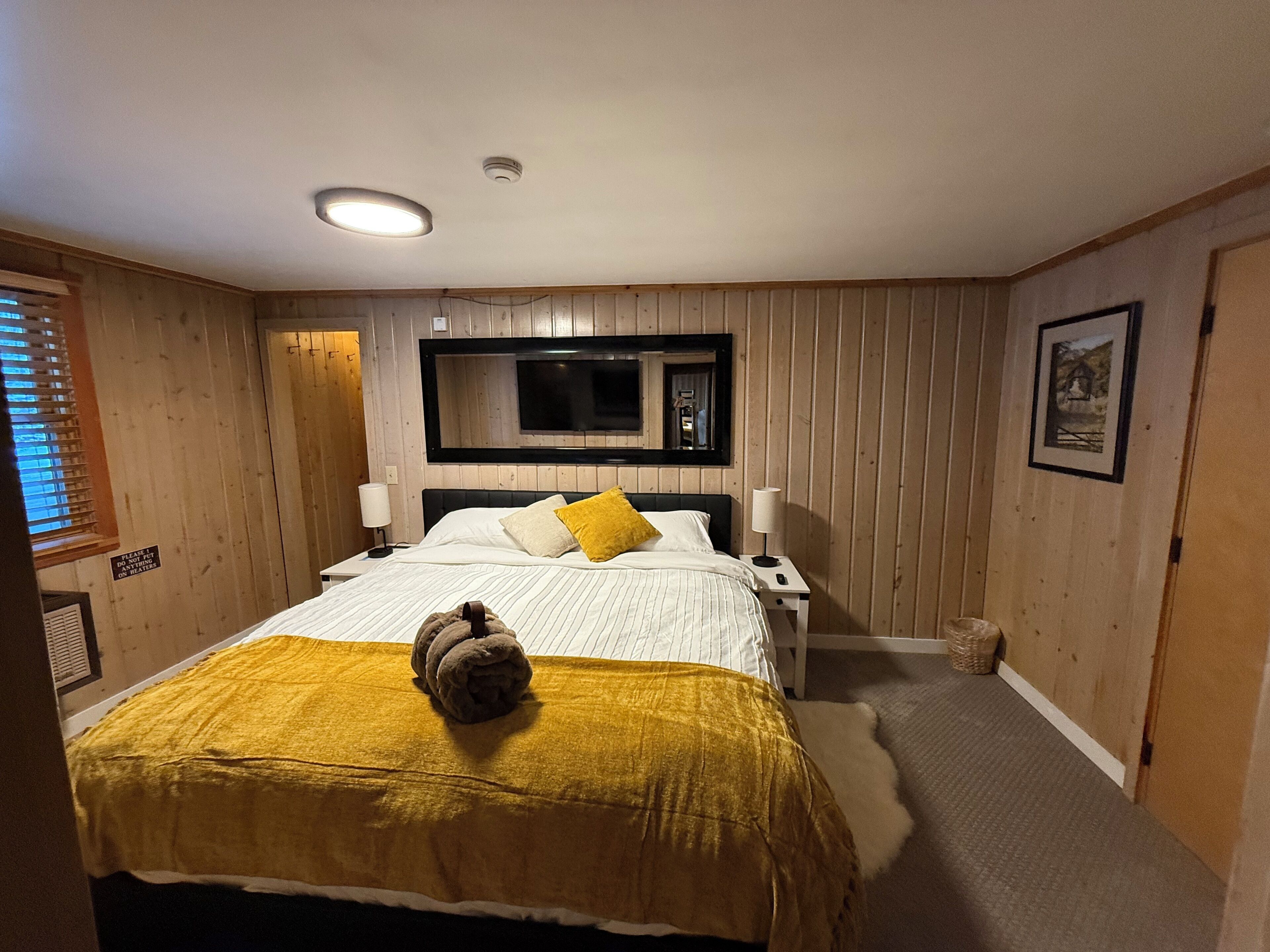 A bedroom with a bed, a television mounted on the wall, a bedside table with a lamp, and a sign on the wall.