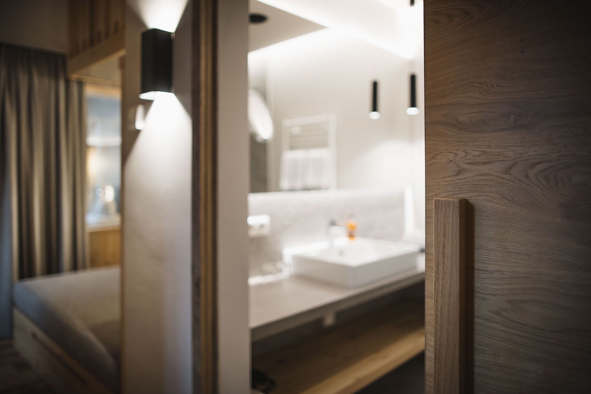 Ein modernes Badezimmer mit einem weißen Waschbecken, einem Spiegel und einer Holztür.