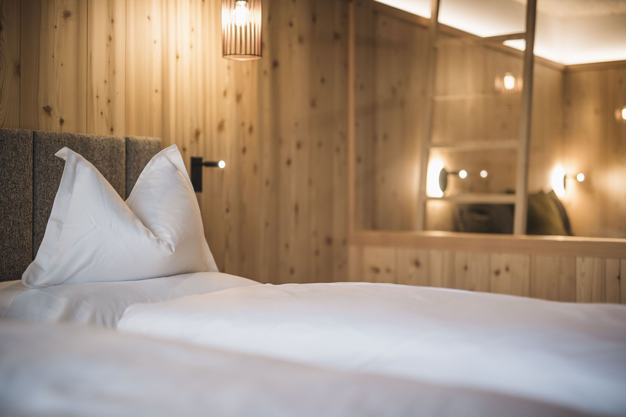 A bed with white linens and two pillows in a room with wooden paneling and a mirror reflecting the room.