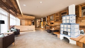A spacious lobby with a reception desk, wooden flooring, and a large blue and white tiled fireplace. - Autentis (Rasun Anterselva)