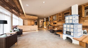 Un'ampia hall con reception, pavimento in legno e un grande camino rivestito di piastrelle blu e bianche.