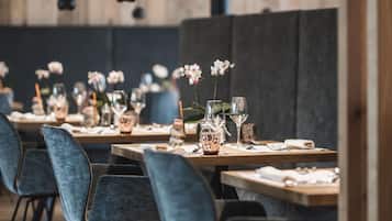 Een restaurant met houten wanden, hangende lampen en blauwe fauteuils. Tafels zijn gedekt met wijnglazen en kleine vazen.