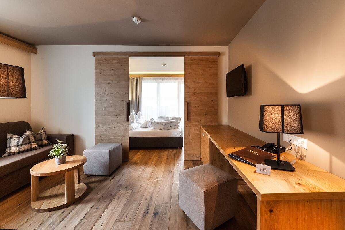 Una habitación de hotel moderna con piso de madera, un sofá, una mesita, un escritorio y una cama con vista a un balcón.