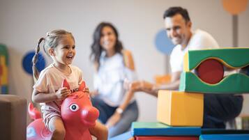 A child on a red toy horse, adults in the background, and colorful building blocks.