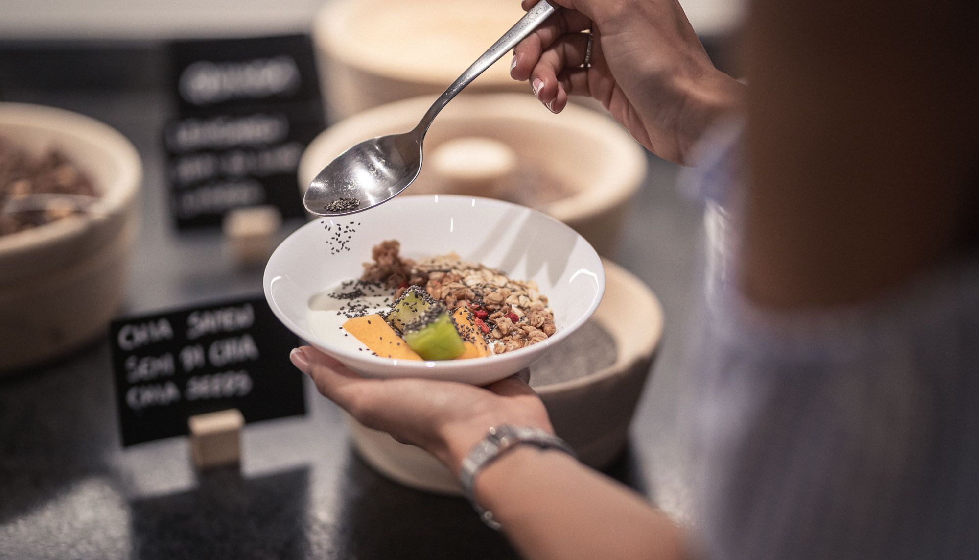 Iemand houdt een kom met een lepel vast en voegt granola toe.