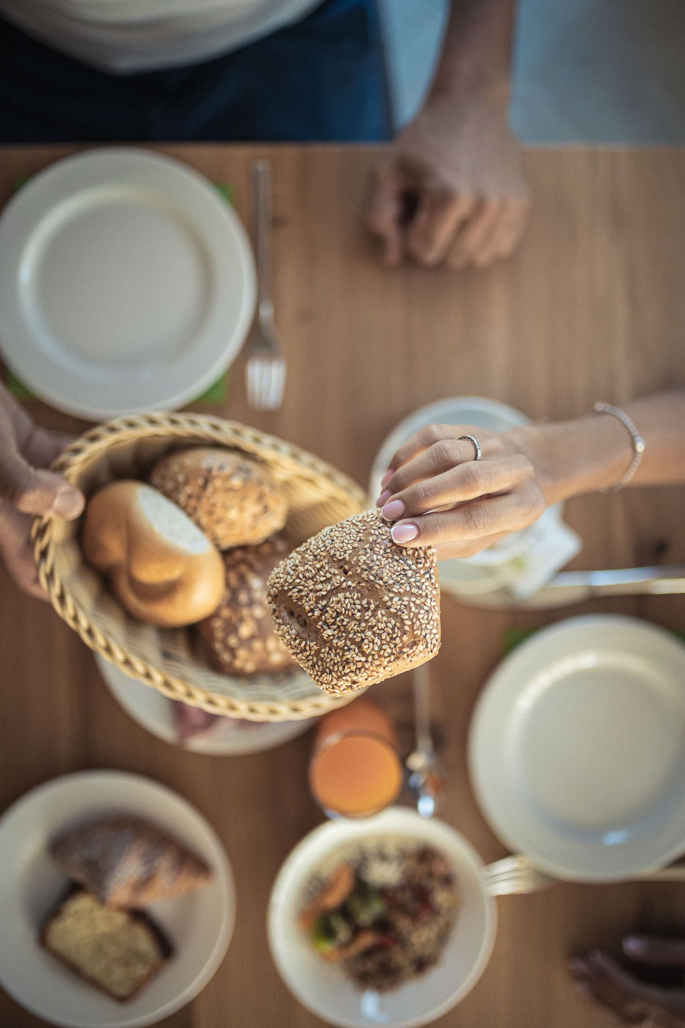 A person holding a basket of bread and a small bowl, with a dining table in the background.
