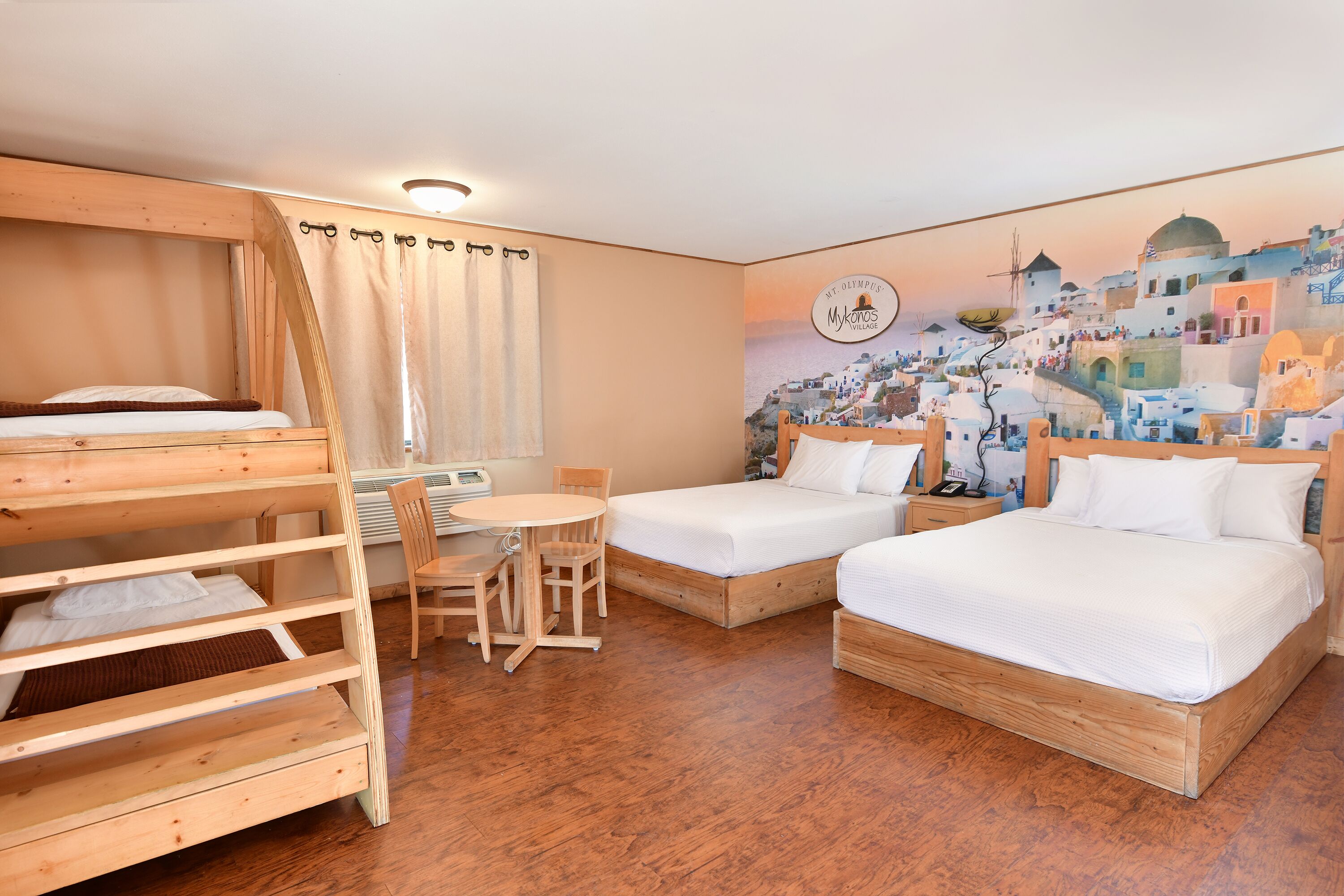 A room with two single beds, a bunk bed, a round table, and chairs.