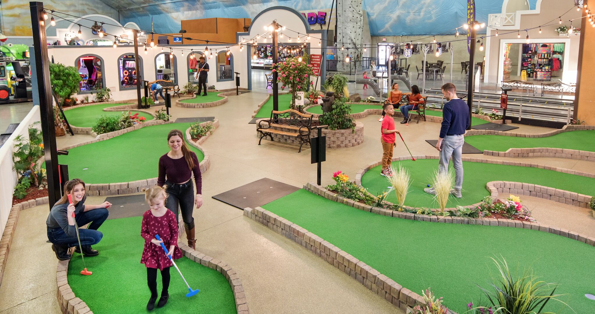 A miniature golf course with artificial turf, benches, and potted plants.