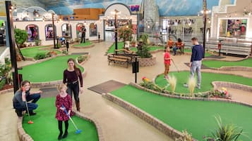 A miniature golf course with artificial turf, benches, and potted plants.