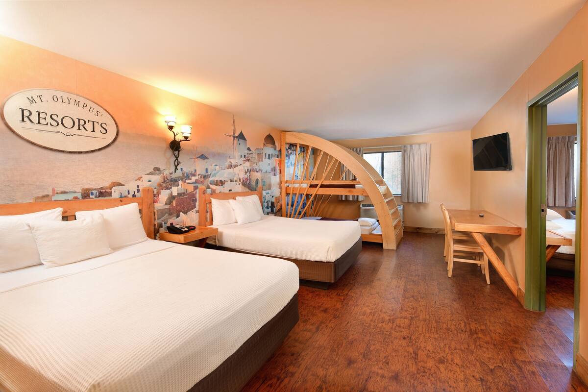A hotel room with two beds, a wooden desk, and a mural of a coastal town.