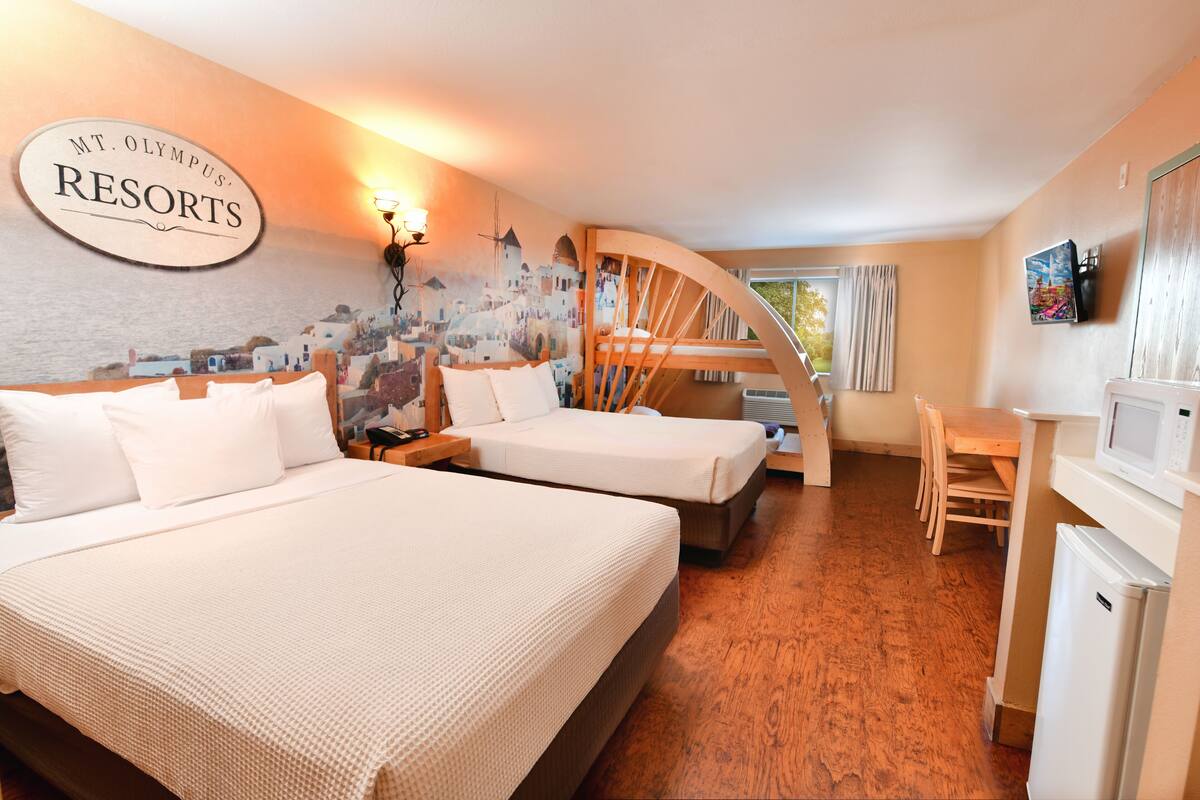 A hotel room with two beds, a wooden staircase, a dining area, and a TV.