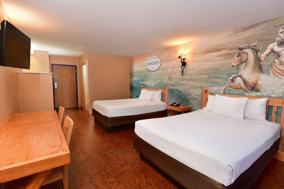 A hotel room with two beds, a wooden table, a TV, and a mural of a horse and rider.