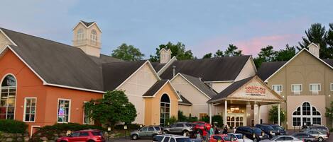 A hotel with a prominent entrance, multiple parking spaces, and a variety of vehicles parked in front.