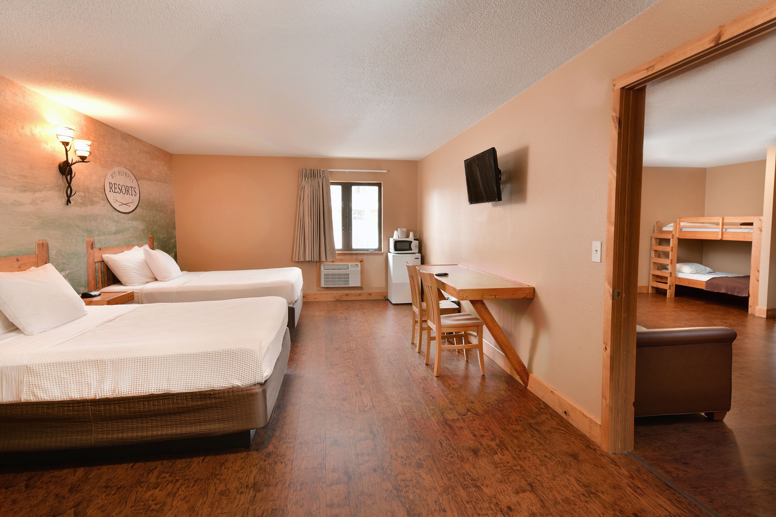 A hotel room with two beds, a desk, a chair, a television, and a window with curtains.